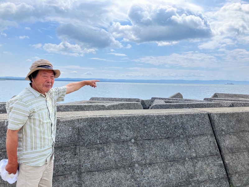 「浮島丸が出港したのはちょうど、あの船のあたり」と指し示す浮島丸下北の会代表の村上準一さん＝青森県むつ市の大湊港で、2025年7月22日、上東麻子撮影