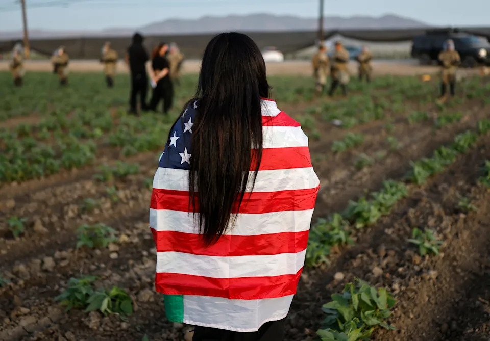 A demonstrator wears an American flag as National Guard soldiers block protestors during an ICE immigration raid at a nearby cannabis farm on July 10, 2025 near Camarillo, California. Protestors stood off with federal agents for hours outside the farm in the farmworker community in Ventura County.