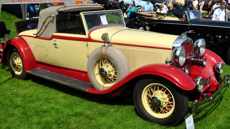 A cream-colored 1931 Lincoln Model K with red accents, parked on grass at a car show