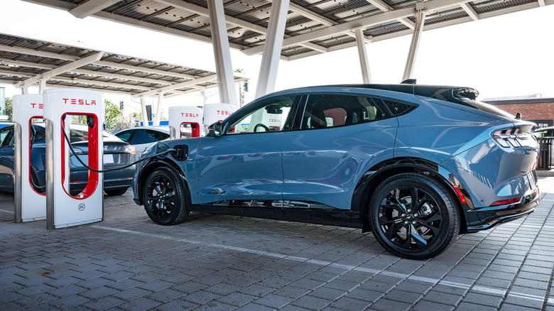 a blue Mustang Mach E charging at a Tesla Supercharger