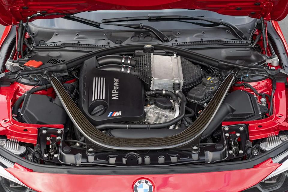 engine bay view showing inline six engine with carbon strut brace and black m power cover under raised hood.