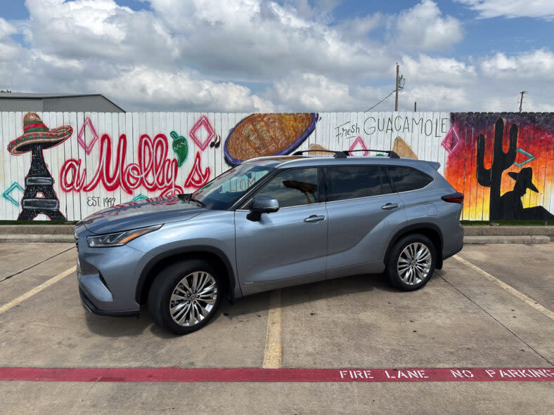A 2024 Toyota Highlander Hybrid parked in front of tasteful Texican graffiti most affordable 3 row SUVs