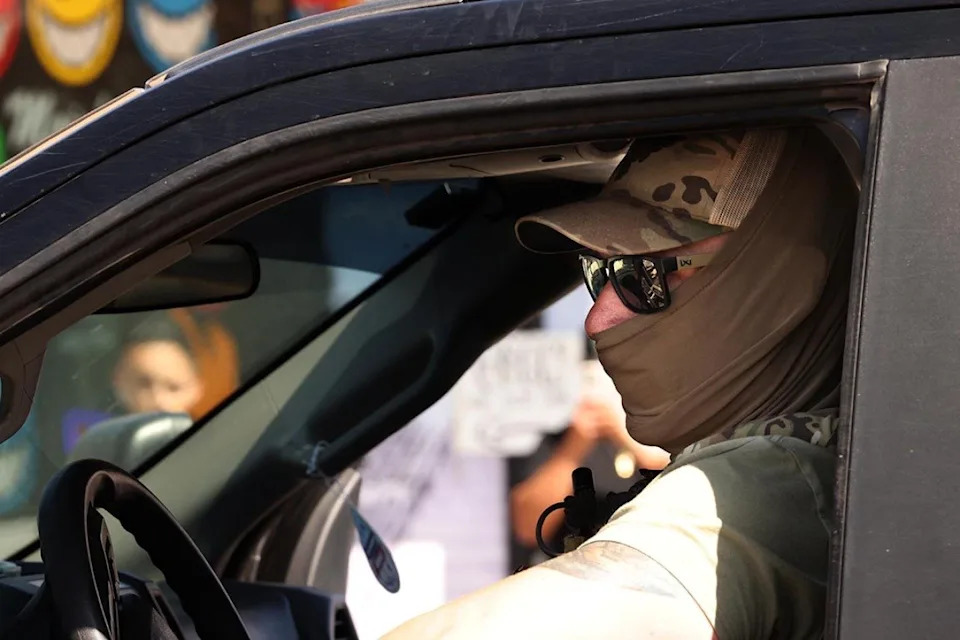 Closeup of a masked federal agent wearing sunglasses and a hat seen through his drivers' side window, planning his escape through an angry crowd after an immigrant raid on Atlantic Boulevard in the city of Bell - Genaro Molina // Los Angeles Times via Getty Images