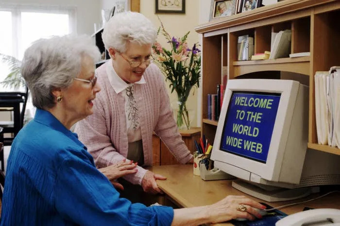 Two elderly women using an old computer, the monitor displays "Welcome to the World Wide Web."