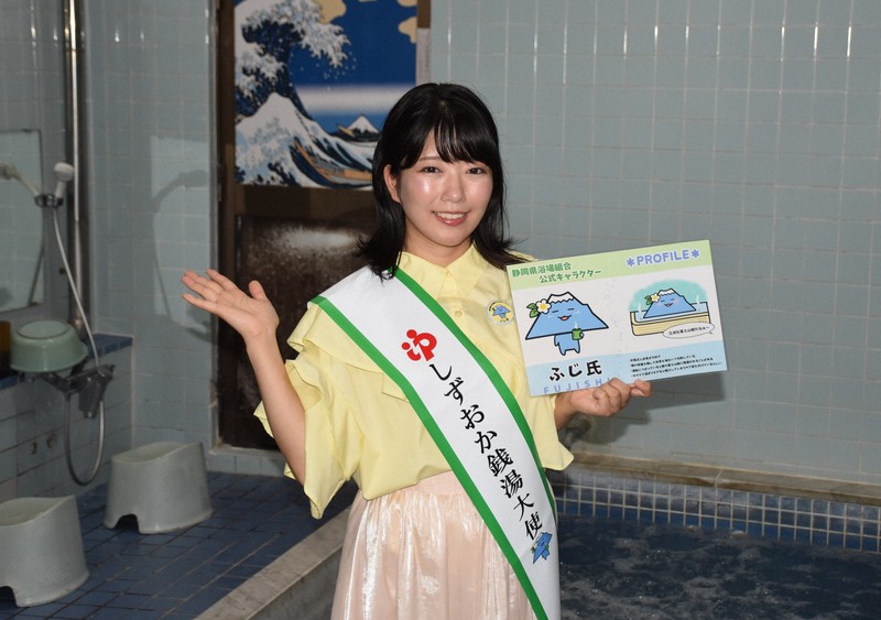 自ら手掛けた公式キャラクターのイラストを手にポーズを取る汐川ほたてさん＝静岡県富士市の「富士見湯」で2025年7月31日午後2時41分、丹野恒一撮影