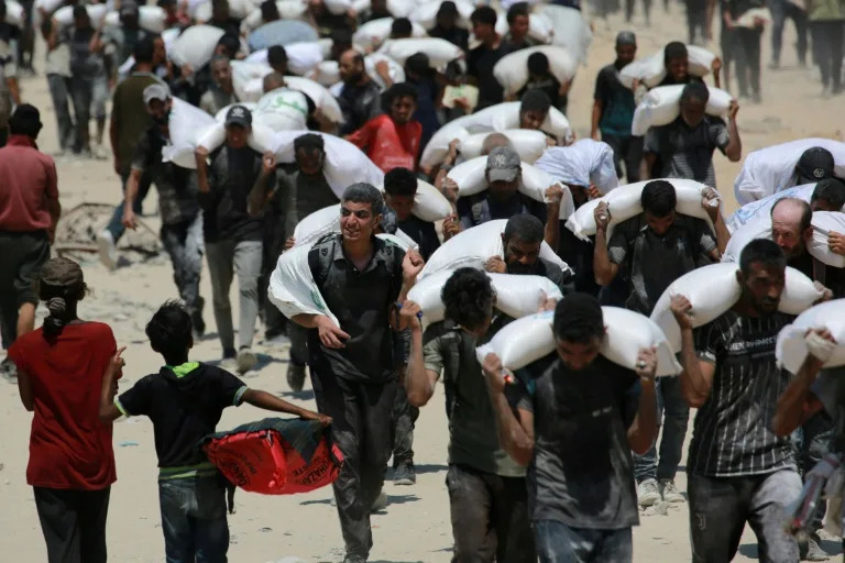Palestinians carrying sacks of flour after trucks carrying humanitarian aid entered northern Gaza (BASHAR TALEB)