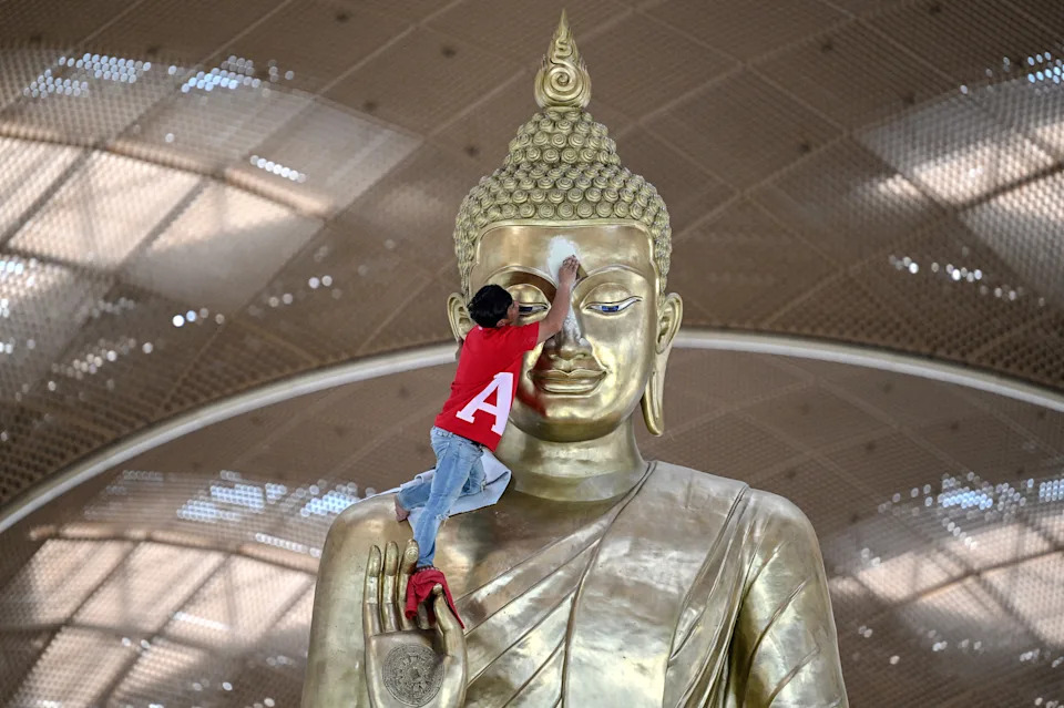 A worker cleans the face of a large statue of Buddha inside an airport.