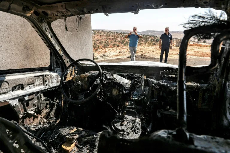 Men stand near a vehicle that was reportedly torched by Israeli settlers during an overnight attack on the Palestinian Christian village of Taybeh (Zain JAAFAR)