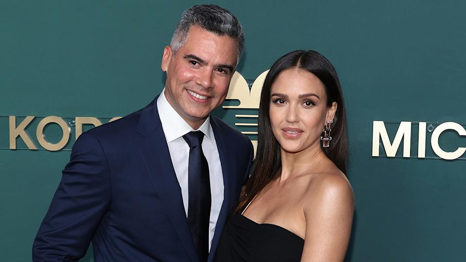 Cash Warren con traje azul marino y corbata posa junto a su mujer Jessica con un vestido negro de tirantes en la alfombra