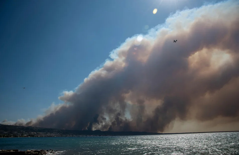 Smoke from a wildfire covers the sky above a seaside village.