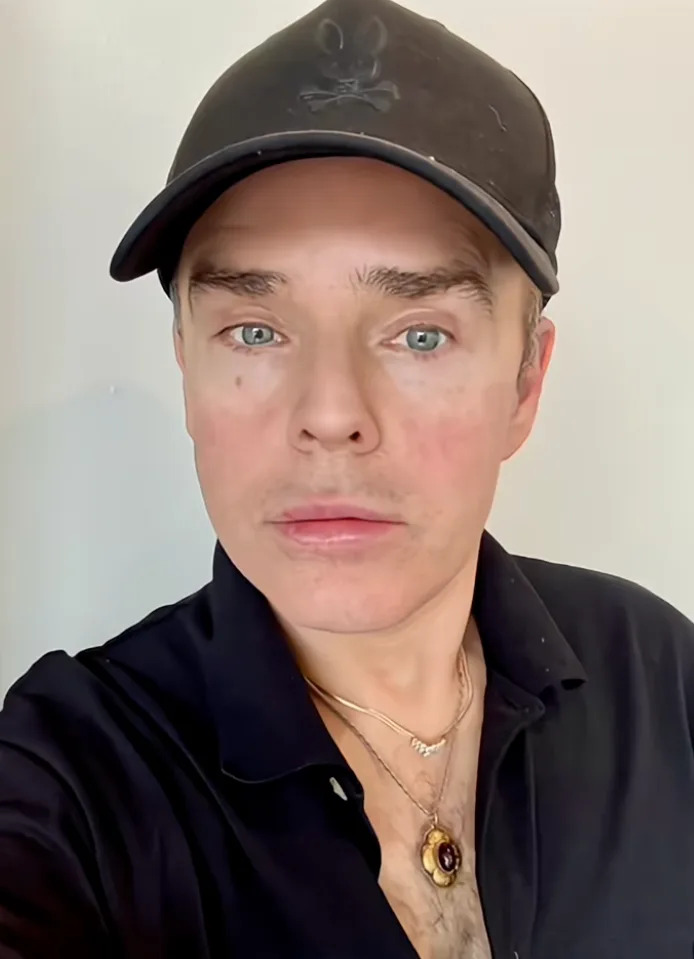 Person with neutral expression wearing a baseball cap and a dark shirt, visible on a phone screen with social media interaction icons
