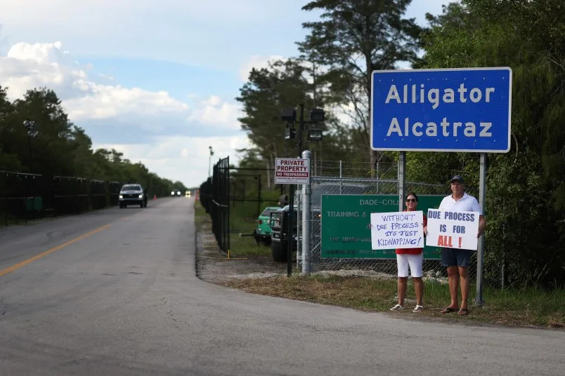 OCHOPEE, FLORIDA – AUGUST 03: Leo and Catherine Gentile hold signs near the entrance to the state-managed immigration detention center dubbed Alligator Alcatraz, located at the Dade-Collier Training and Transition Airport in the Florida Everglades on August 03, 2025 in Ochopee, Florida. Faith leaders led prayer for those being held within the facility. (Photo by Joe Raedle/Getty Images)