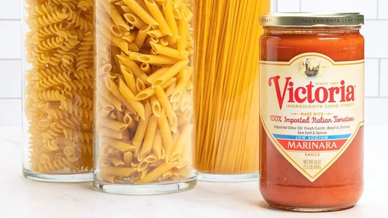 Jar of Victoria marinara beside containers of pasta before a white tile backsplash