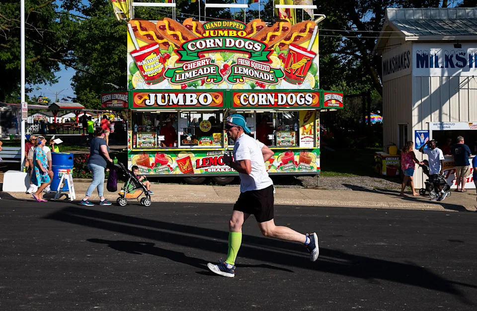 Runners in the Illinois State Fair Parade Run pass by the corn dog stand on Main Street as they near the finish line prior to the Illinois State Fair Twilight Parade on Aug. 9, 2018, at the fairgrounds in Springfield, Ill.