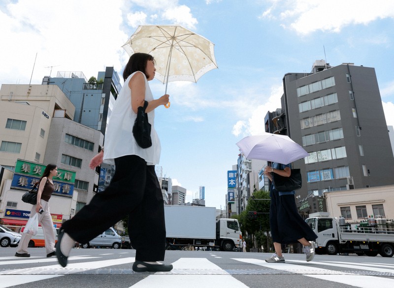 照りつける日差しの中で日傘を手に歩く人たち＝東京都千代田区で2025年7月18日、滝川大貴撮影