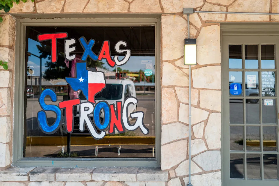 a window decoration says 'texas strong' with a drawing of the state flag in the shape of Texas. The decoration appears in the window of a stone business