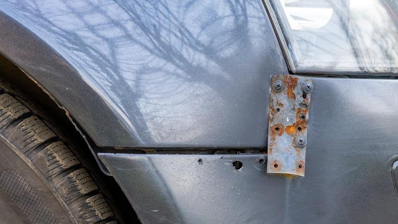 A car bumper repair on a silver vehicle using a rusty metal plate and screws
