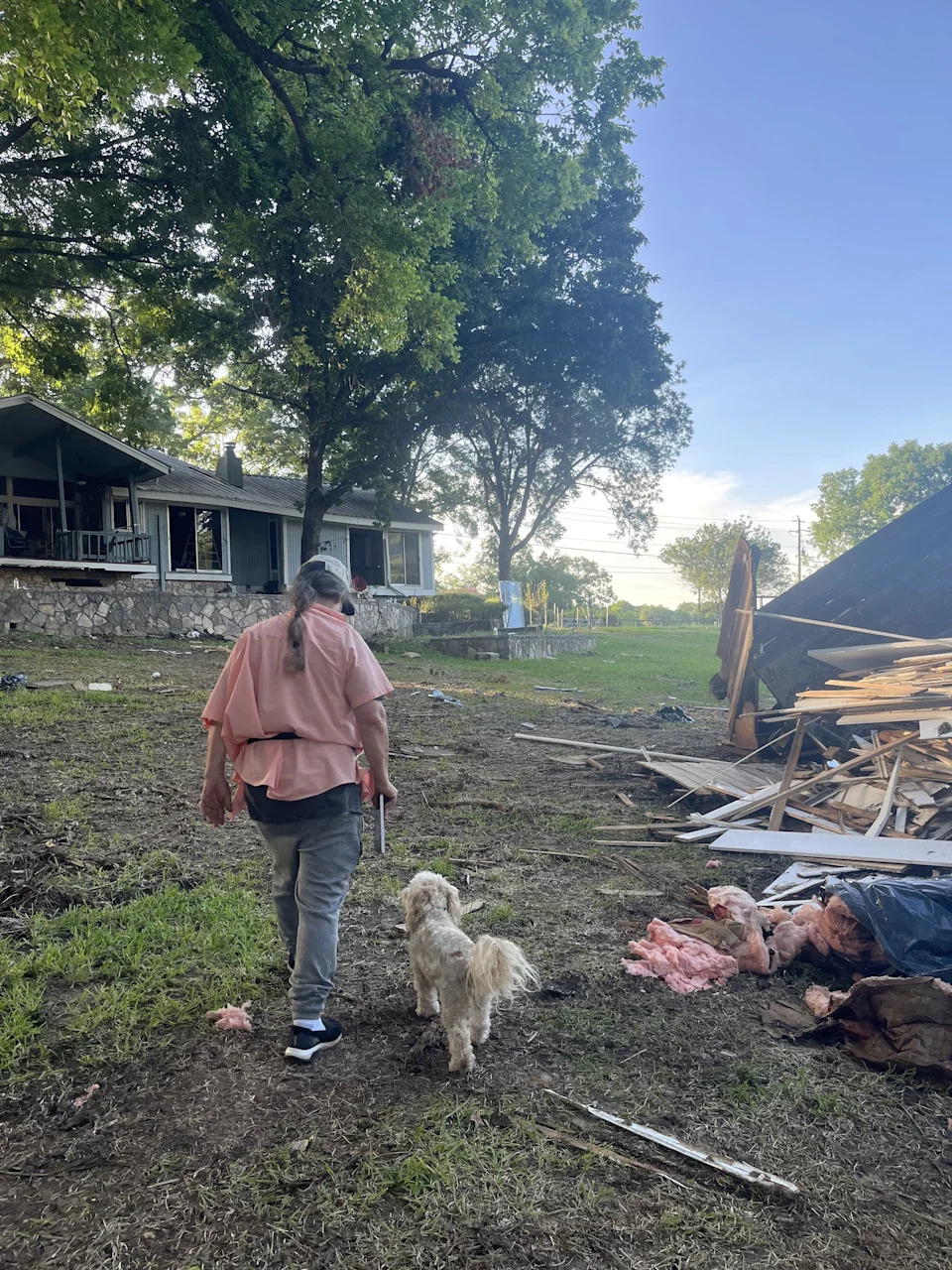 a man and his dog walk near a pile of debris and a house after a flood