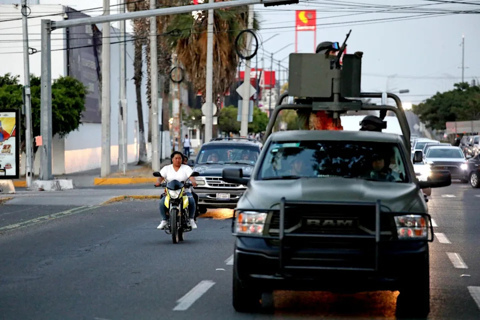 Soldiers patrol the street in a vehicle.