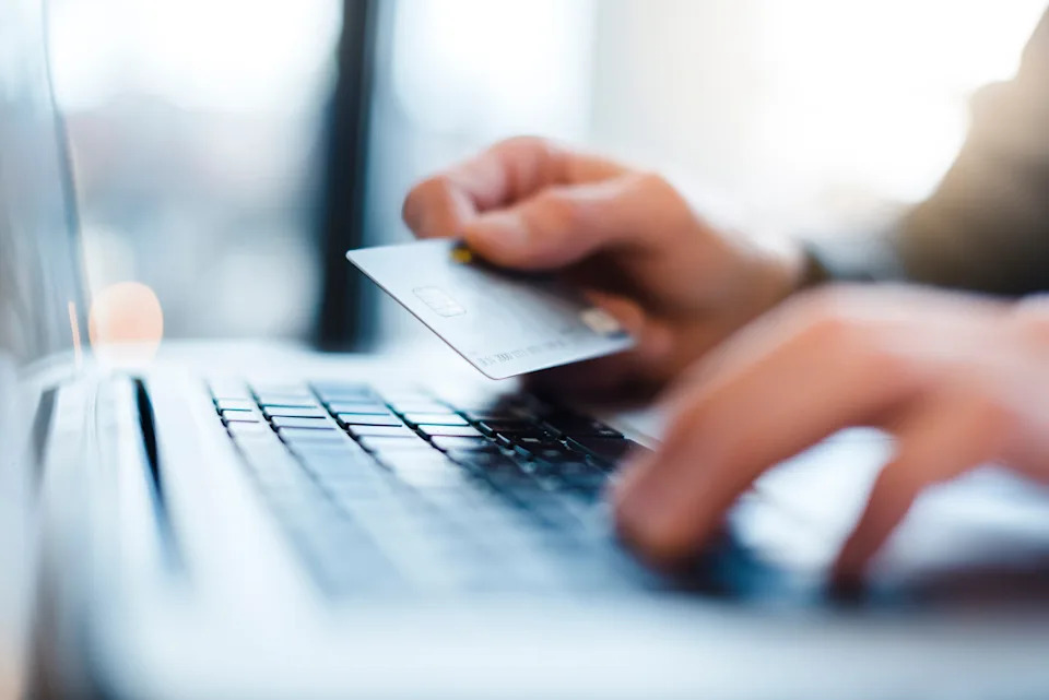 Person holding a credit card in one hand while typing on a laptop keyboard, portraying online shopping or banking activities