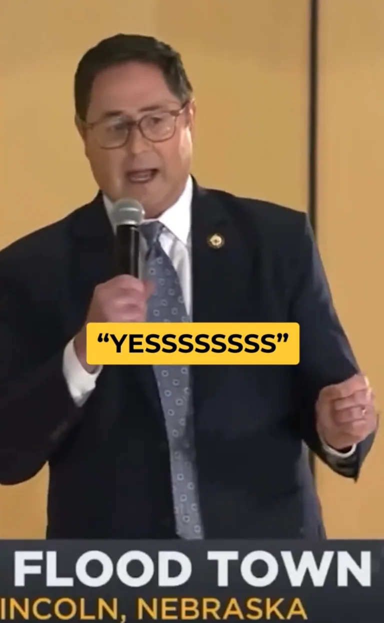 Man in a suit and tie holding a microphone with the caption "YESSSSSSS" superimposed