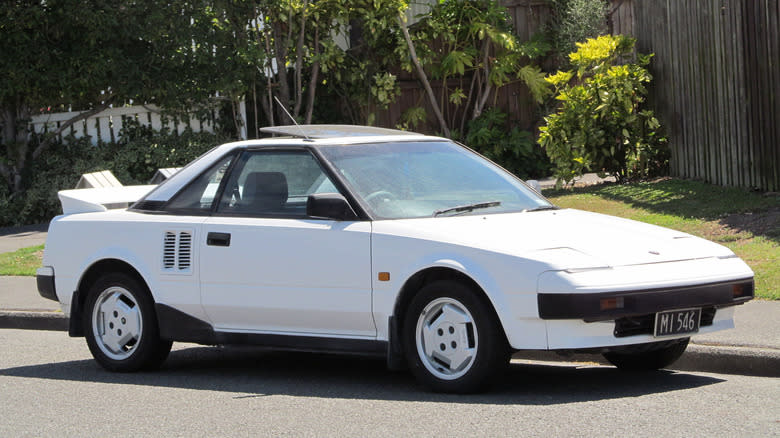 A white 1985 Toyota MR2 parked in front of trees