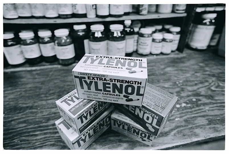 Boxes of Extra-Strength Tylenol capsules are stacked on a wooden counter with more medicine bottles in the background