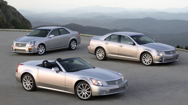 A silver Cadillac CTS-V, STS-V, and XLR-V parked in front of a mountain range