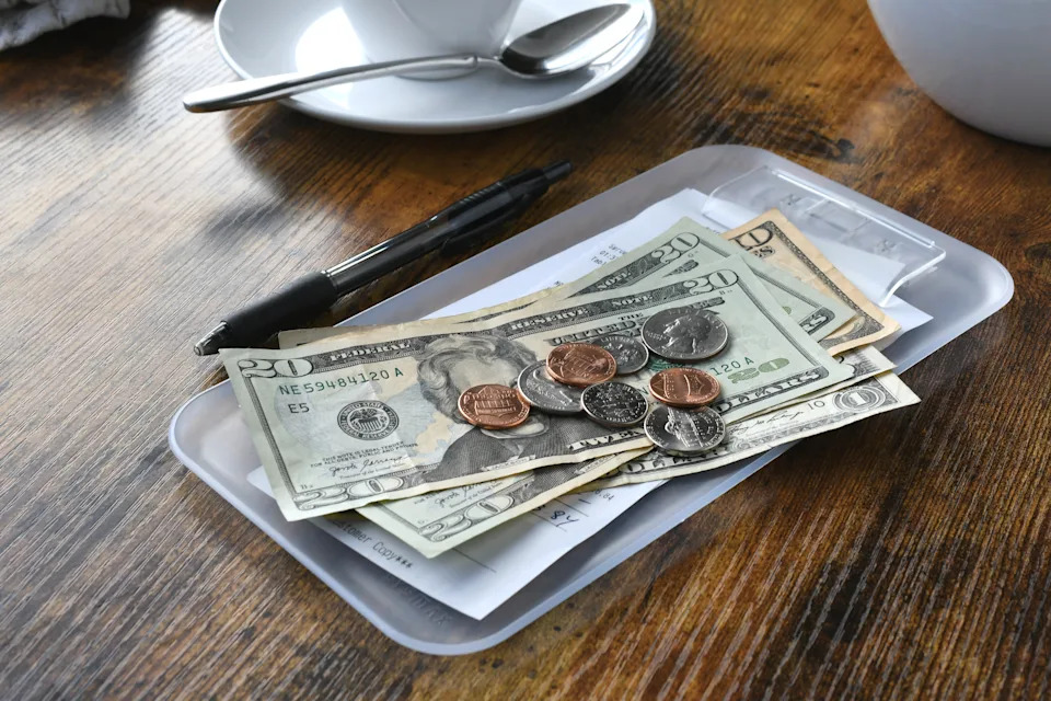 Tip tray with a pen, receipts, and various U.S. dollar bills and coins on a wooden table