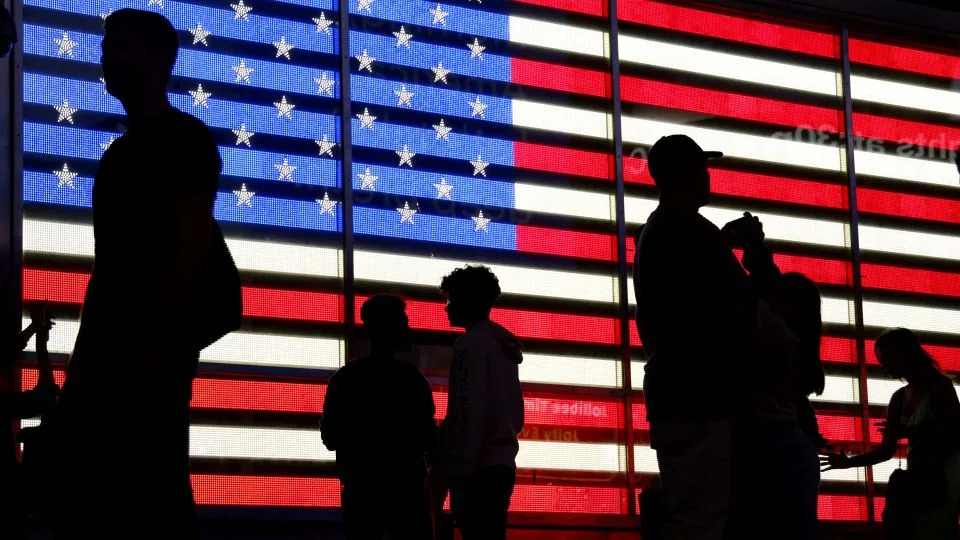 People stand in front of a US flag on a screen in Times Square in New York on September 19, 2022. - Ludovic Marin/AFP/Getty Images