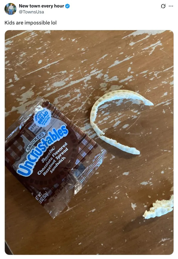 Half-eaten sandwich crust on a table next to an open Uncrustables wrapper, with text above saying "Kids are impossible lol."