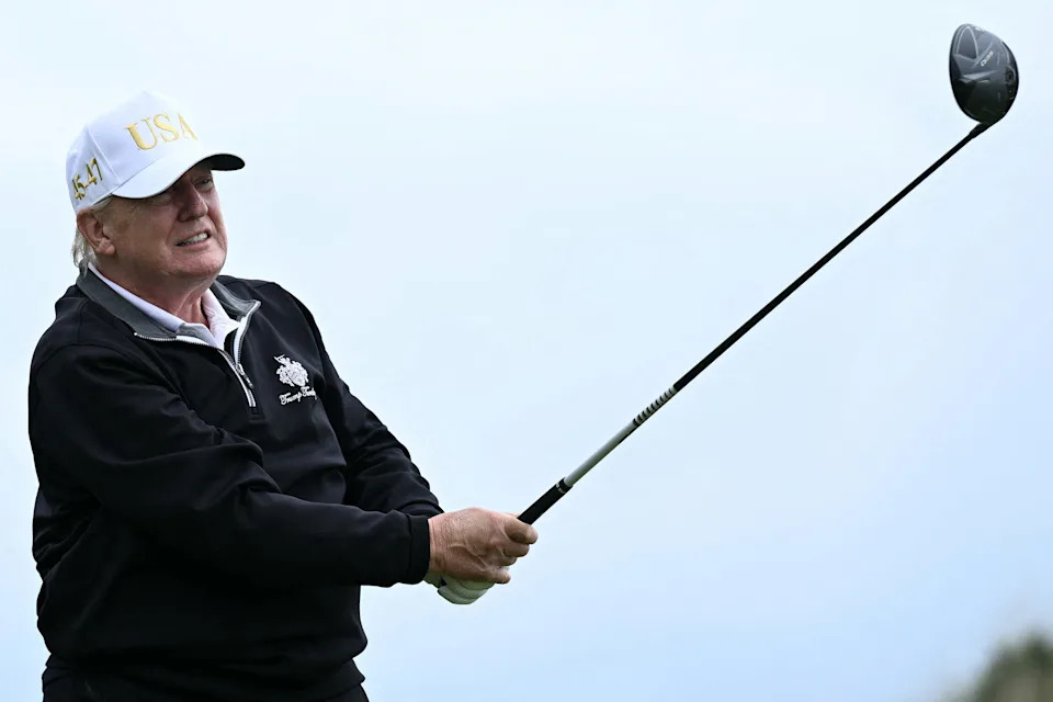 Person swinging a golf club on a course, wearing a hat and sweater with "USA" visible on the cap