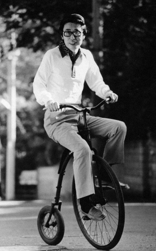 ミウラート・ヴィレッジで展示する、クラシックな「だるま自転車」に乗る真鍋の写真（1975年ごろ）。真鍋は（構想中の）瀬戸大橋に自転車道を、と考えていた＝愛媛県美術館蔵