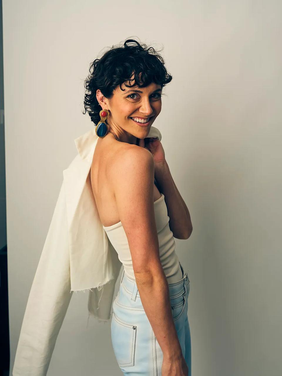 Alyson Stoner con un top de tubo blanco y pantalones a juego sonriendo con una americana al hombro.