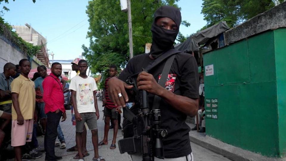 Un hombre con un rifle delante de otros hombres en un barrio de Puerto Príncipe