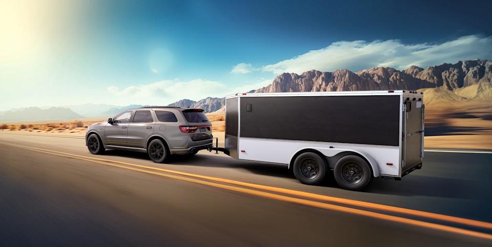 rear three quarter view of gray suv towing enclosed trailer on desert highway with mountains in background.
