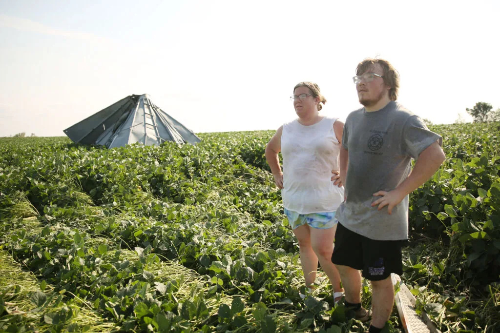 Amanda Lounsbery (left) and her son Hayden Lounsbery survey damage to their family's soybean fields on July 29, 2025. Their grain bin carved a path into the field and split into two pieces after a storm system moved through the area the previous evening. The system damaged trees, homes and other structures. (Makenzie Huber/South Dakota Searchlight)