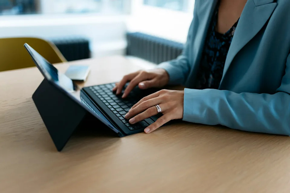 Person typing on a tablet with a keyboard case at an office desk, wearing a suit jacket
