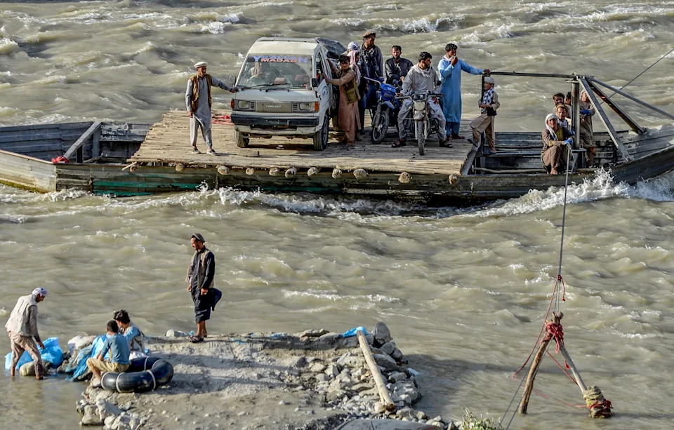 A group of people stand beside a small truck on a small wooden ferry , making their way across a swift-flowing river.
