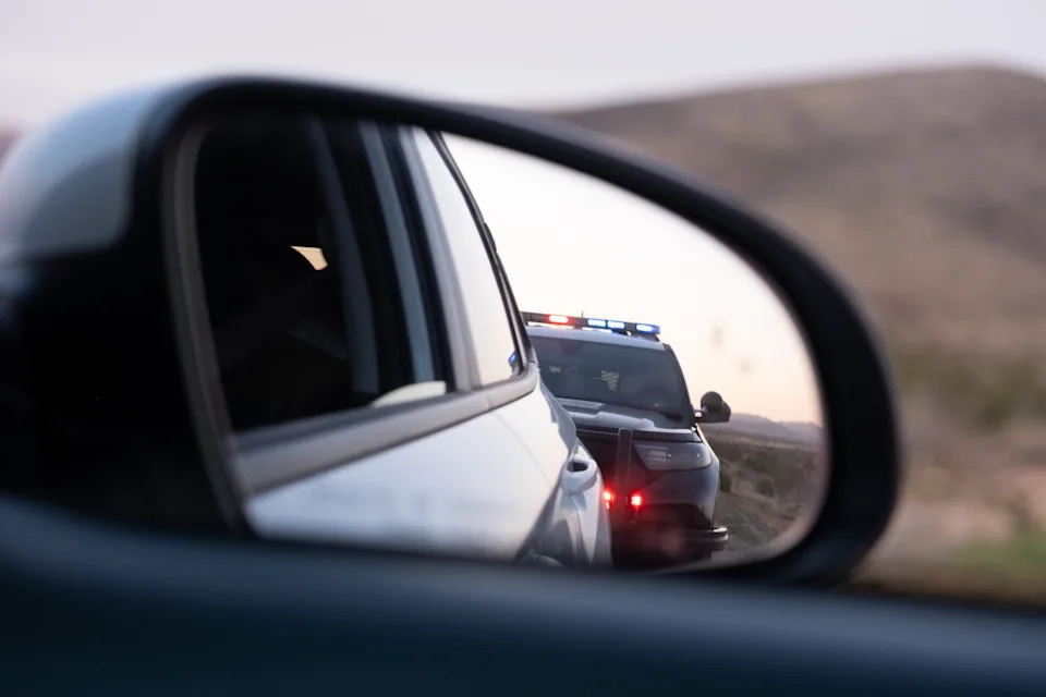 Police car with flashing lights seen in rear-view mirror, suggesting a traffic stop on a highway