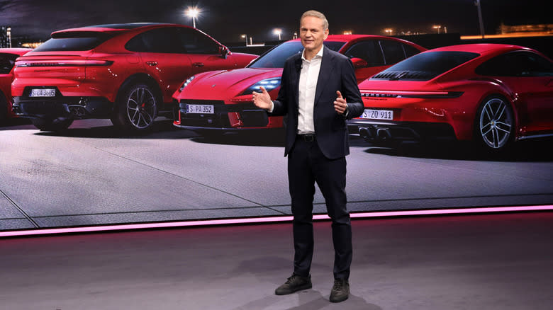 Porsche CEO Oliver Blume standing front of red Porsche vehicles.