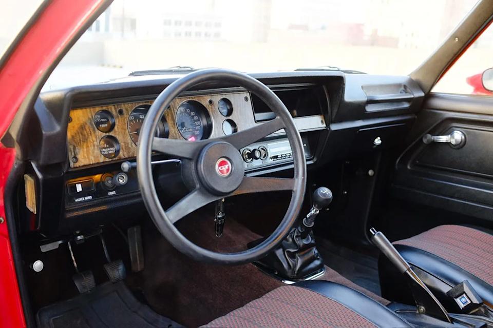 interior view from driver side seat showing three spoke steering wheel, woodgrain dash panel, manual gear shifter, and analog gauges.