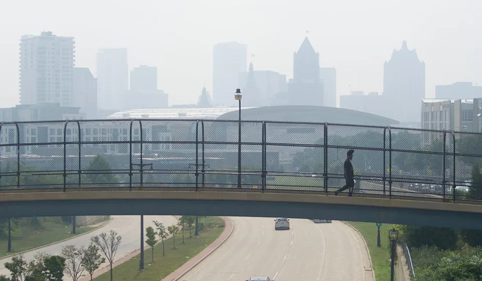 Martrell Lewis of Milwaukee crosses the pedestrian bridge over West McKinley Avenue to West Winnebago Street as a blanket of smoke fills the air from Canadian wildfires in Milwaukee on July 31, 2025.