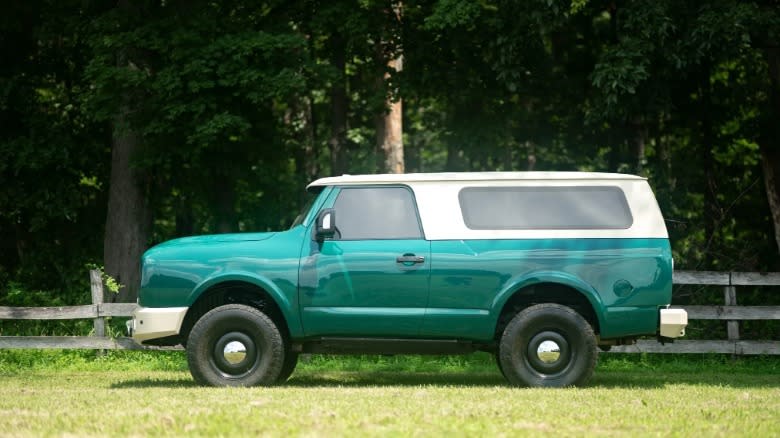 a side view of the green and white Nissan Titan International Scout thing parked on grass in front of trees