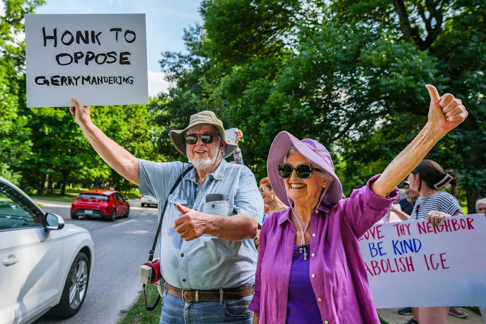 Mike Cabat (left) and Susan Bettis greet cars passing by Thursday, Aug. 7, 2025, outside of the Indiana Governor’s residence on North Meridian Street in Indianapolis. Around 300 stood on the sidewalk to object to the idea of a special session for redistricting in Indiana.