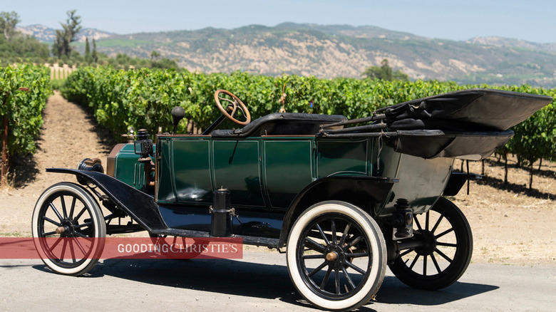 A green 1913 Ford Model T Touring parked in front of grape vines