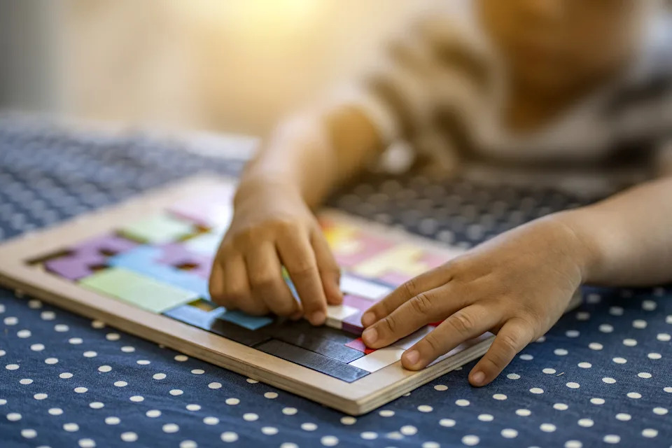 Child assembling a geometric puzzle on a dotted cloth-covered table, focusing on hand-eye coordination and problem-solving skills
