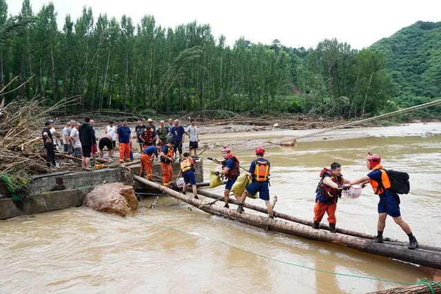 Firefighters transport supplies through a temporarily built wooden bridge at Liulimiao Town in Huairou District in Beijing on July 28