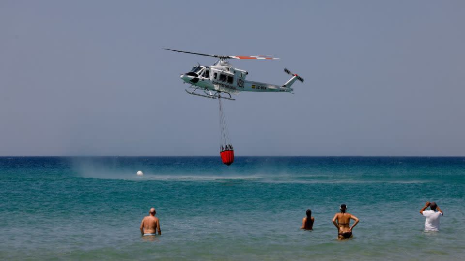 La gente observa cómo un helicóptero extrae agua en la playa de Atlanterra el 12 de agosto de 2025, un día después de que muchas personas, incluyendo residentes y turistas, fueran evacuadas de Tarifa debido a los incendios forestales. - Marcelo del Pozo/Reuters
