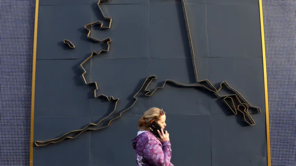 Una mujer con un teléfono celular camina junto a un mapa de Alaska el 9 de julio de 2022 en Anchorage, Alaska. - Justin Sullivan/Getty Images